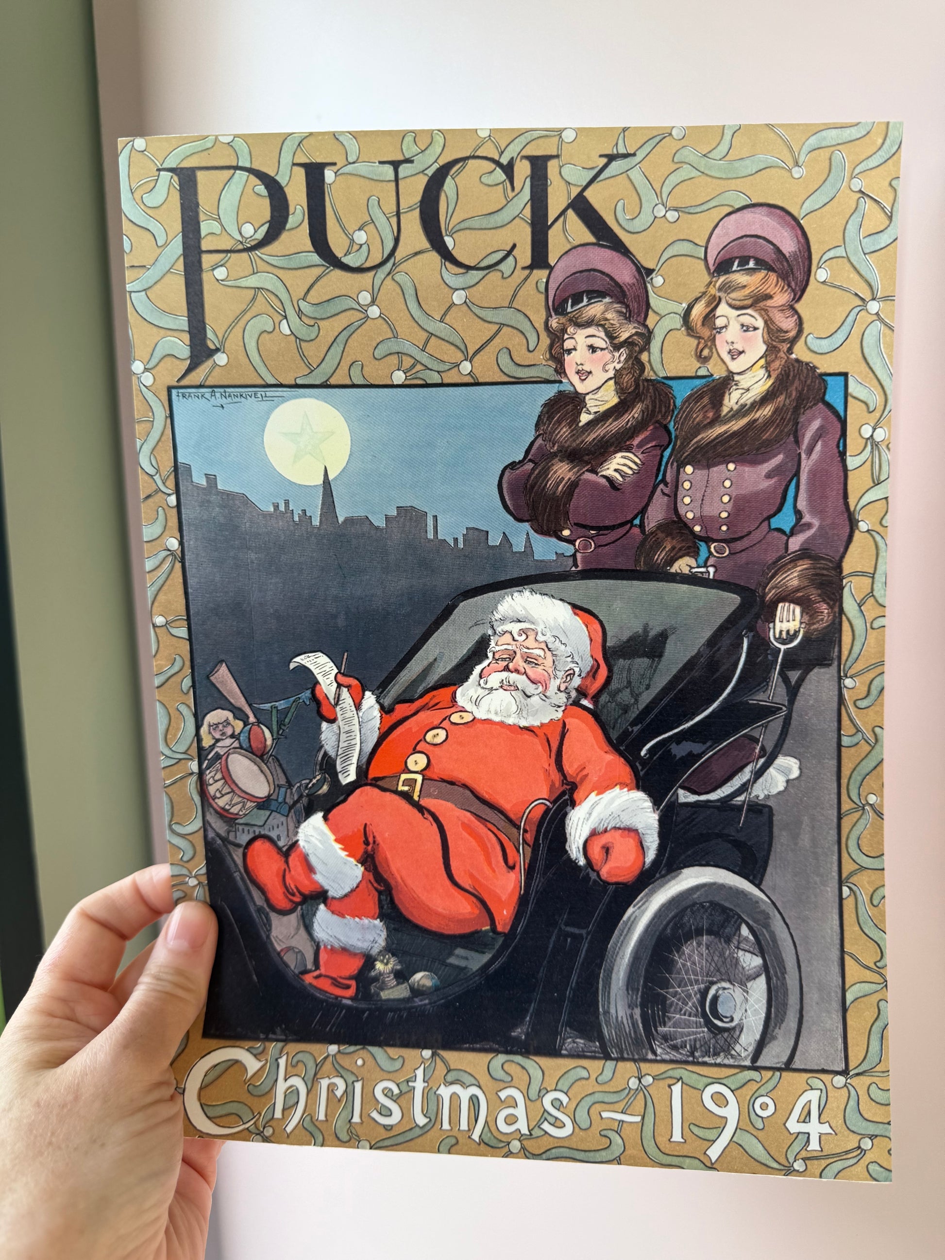 Vintage-style Christmas poster with Santa Claus and two children, held by a hand.