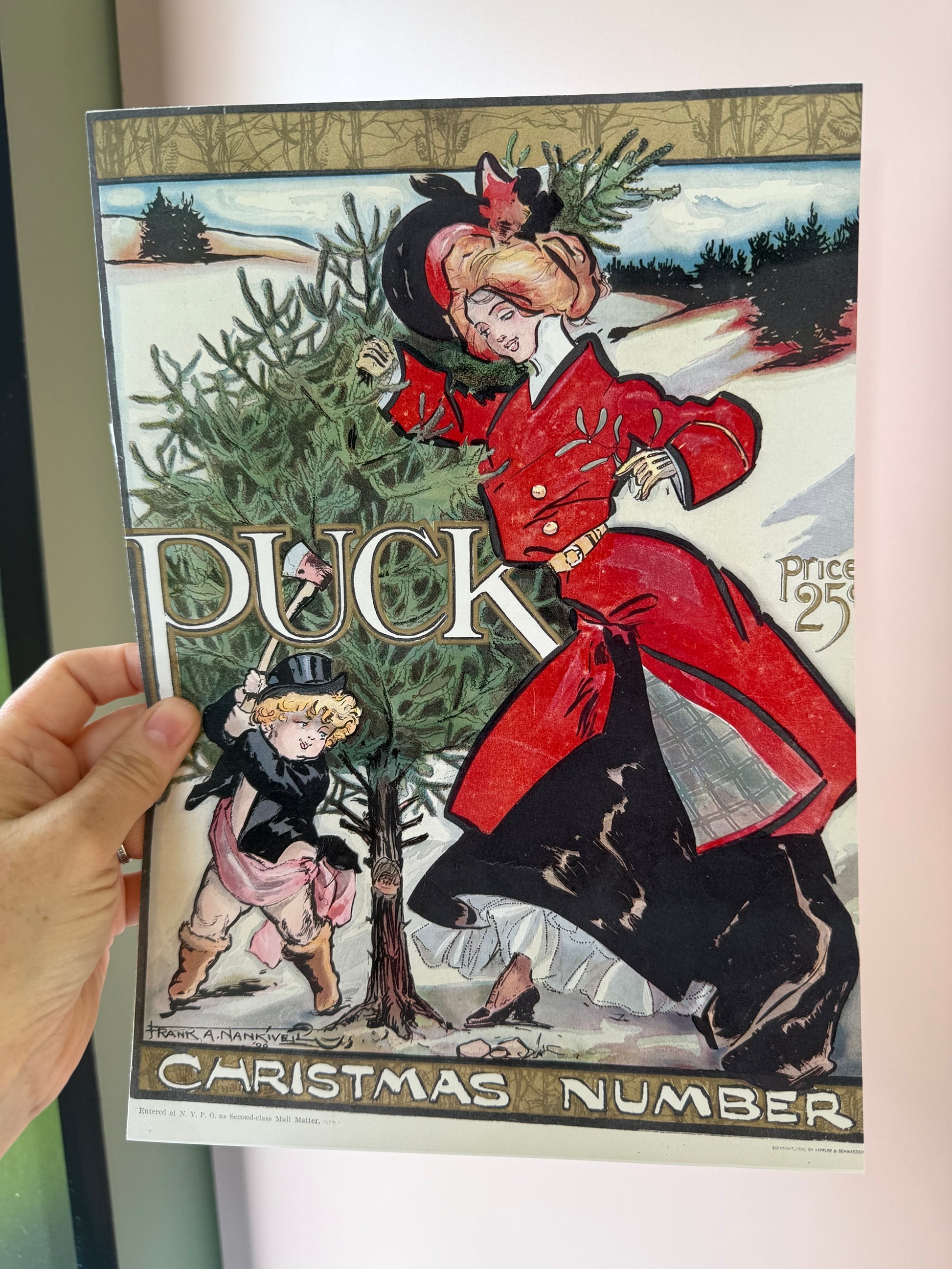 Person holding a magazine with a Christmas-themed cover featuring illustrations of people and trees.
